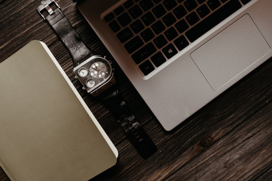 Elegant flat lay of a laptop and watch on a rustic wooden desk, ideal for productivity themes.