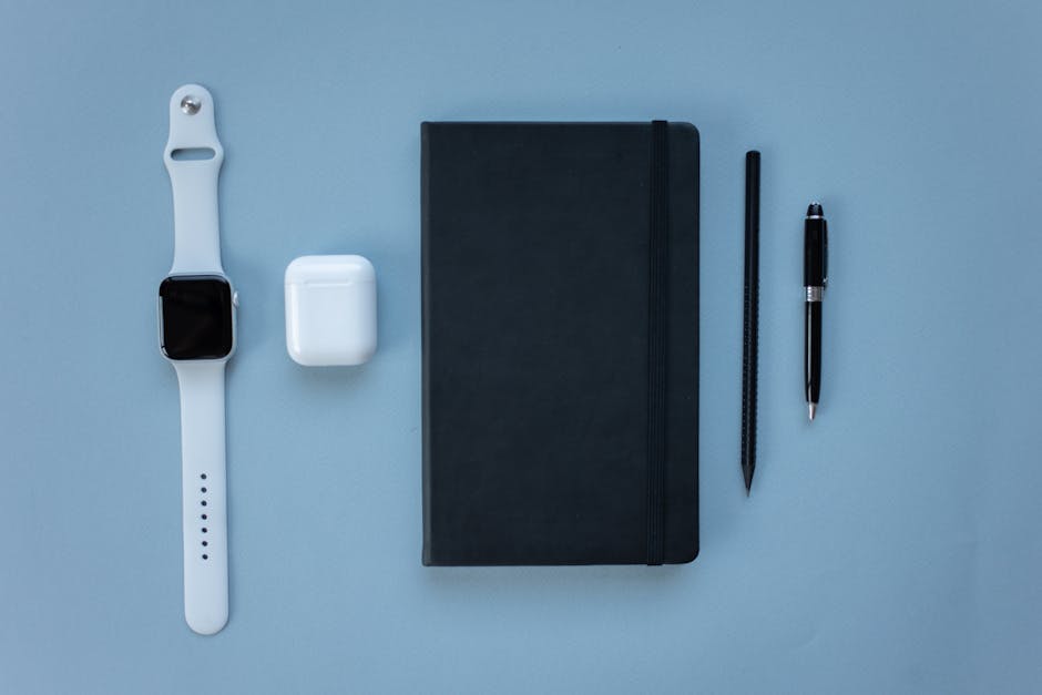 Minimalist flat lay featuring a smartwatch, notebook, and writing tools on a blue background.