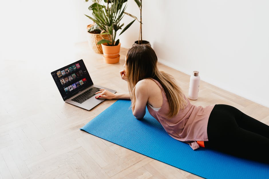 A young woman lying on a yoga mat, browsing on her laptop, enjoying leisure time indoors.