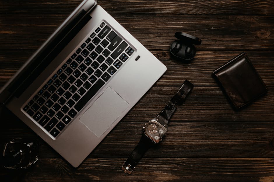 A modern flat lay of a laptop, wristwatch, wallet, and earphones on a wooden table.