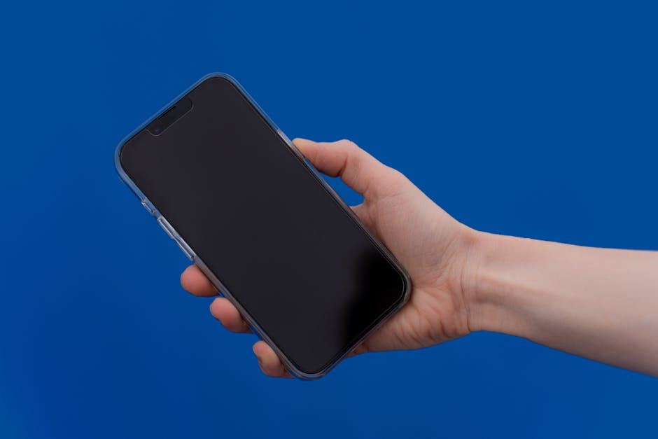 Close-up of a hand holding a smartphone against a bright blue background, showcasing modern technology.
