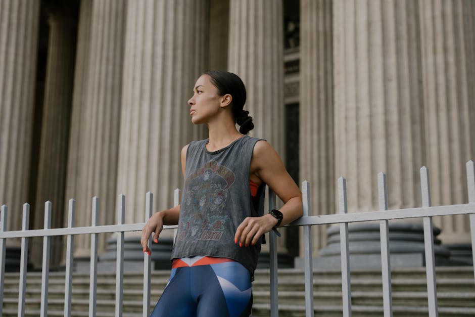Woman in athletic wear leaning on a railing in front of classical columns.