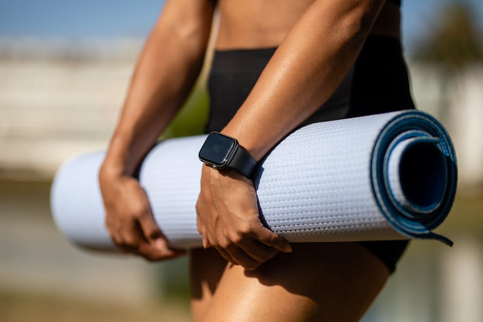 Close-up of a person holding a yoga mat outdoors while wearing a smartwatch, ready for a workout.
