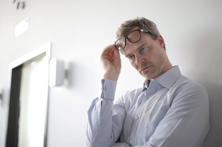 Thoughtful businessman adjusting glasses in a modern office setting, appearing pensive and focused.