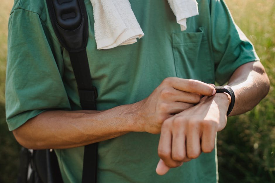 Close-up of a man wearing a green t-shirt using a smartwatch outdoors, with a backpack and towel on his shoulder.