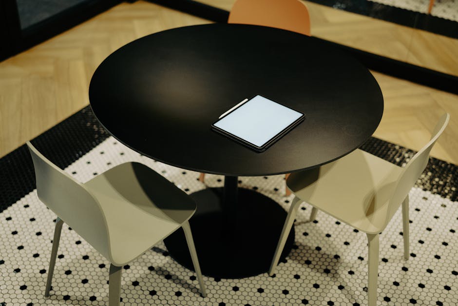 A neatly arranged office space featuring a tablet on a round table with minimalistic chairs.