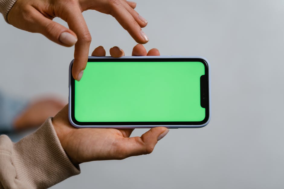 Two hands using a smartphone with a green screen, ideal for mockups.