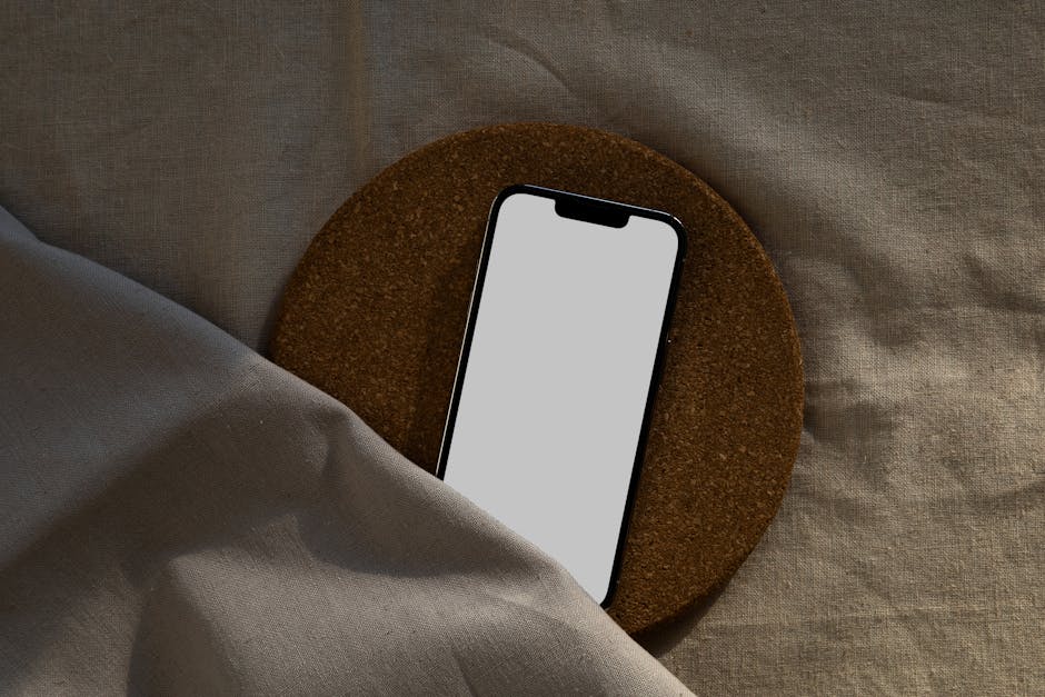 A smartphone with a blank screen on a circular cork surface over a fabric background.