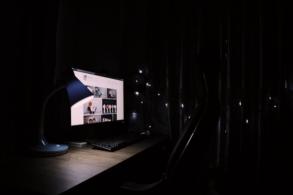 A dimly lit home office desk with a glowing computer monitor and decorative lights creating a cozy atmosphere.