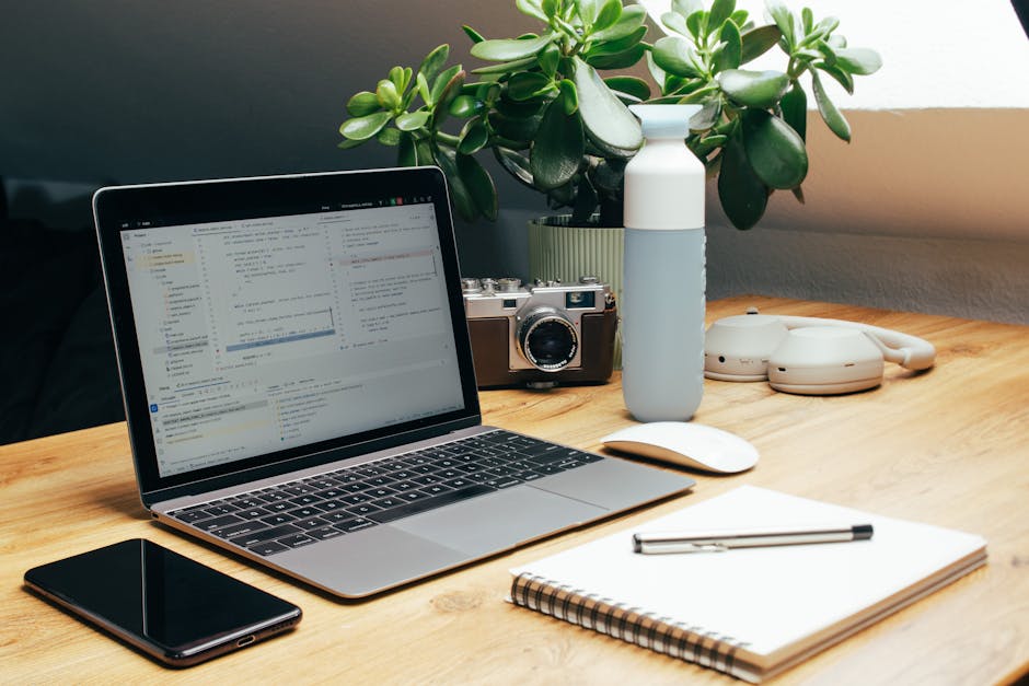 Cozy home office setup with laptop, camera, and plant on a wooden desk.