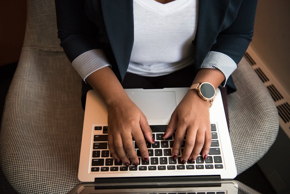 Woman typing on a laptop while seated indoors, showcasing technology and modern work habits.